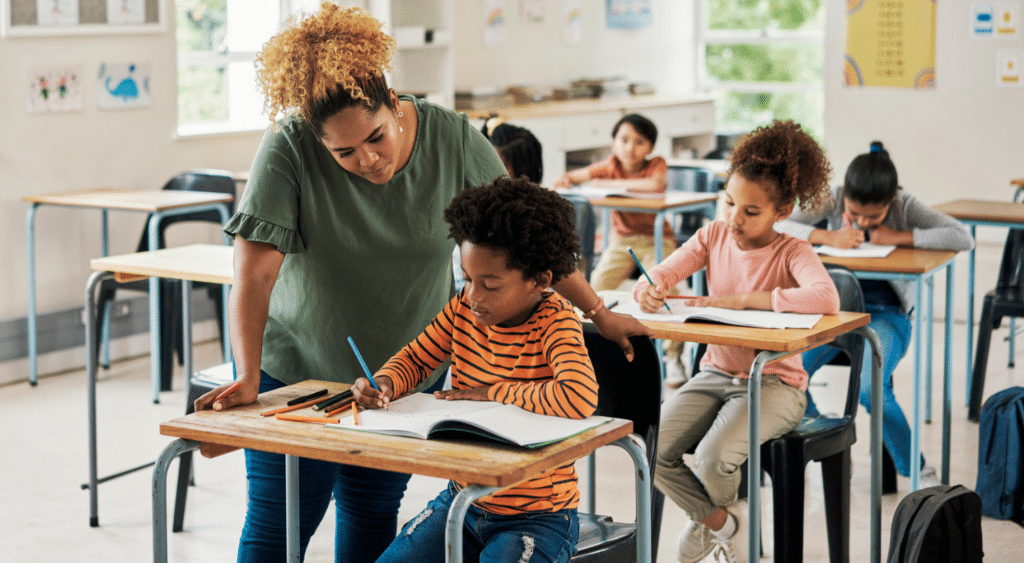 A teacher helping her student with assignments, in a classroom.