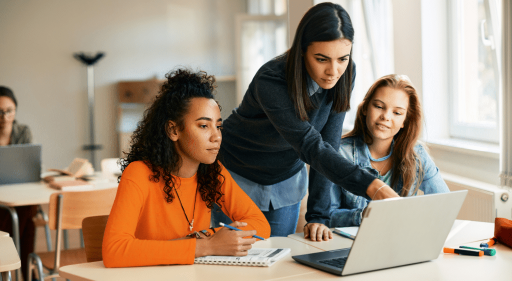 a teacher shows Homework to two students on a computer.