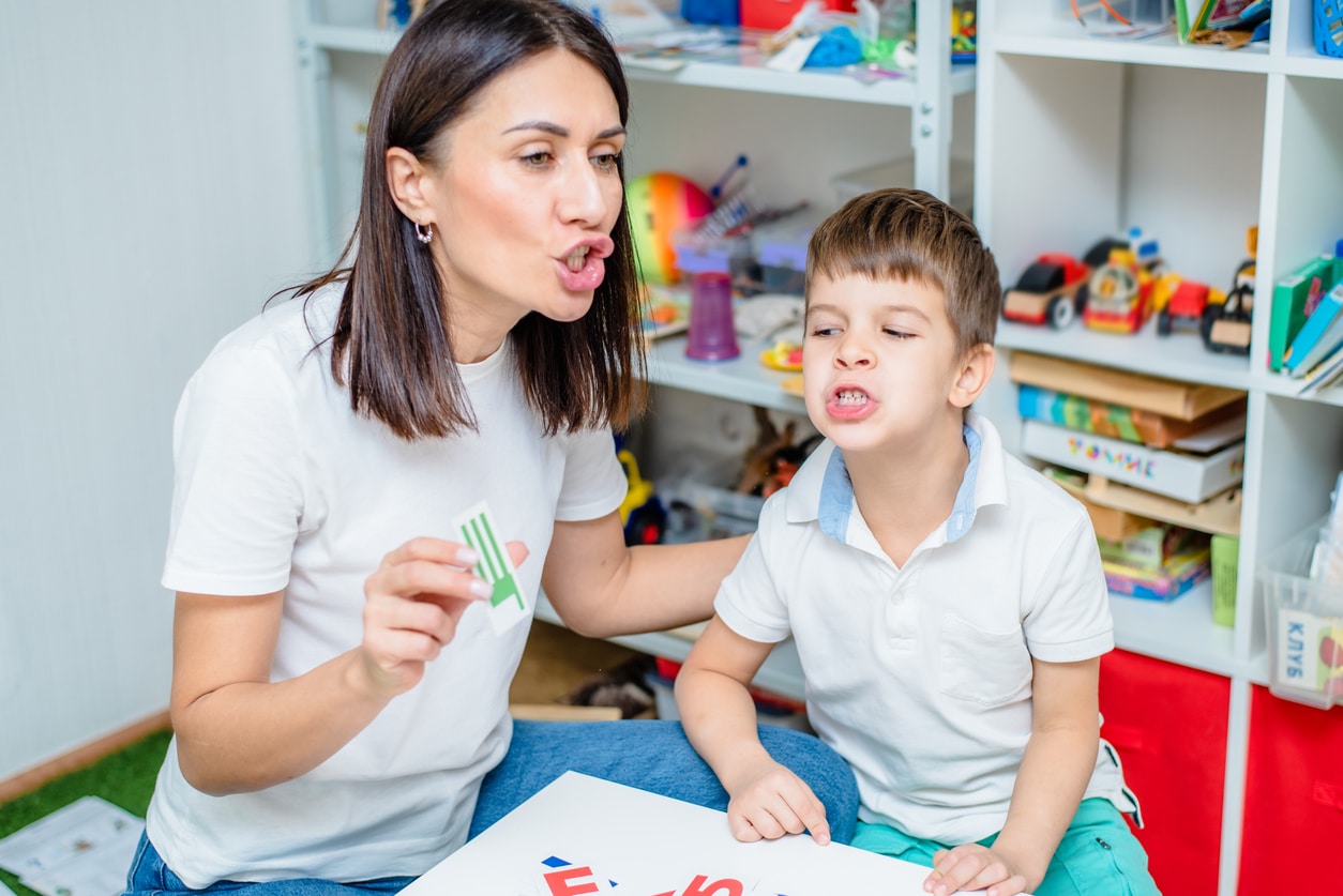 Woman speech therapist teaches boy the correct pronunciation of words and sounds