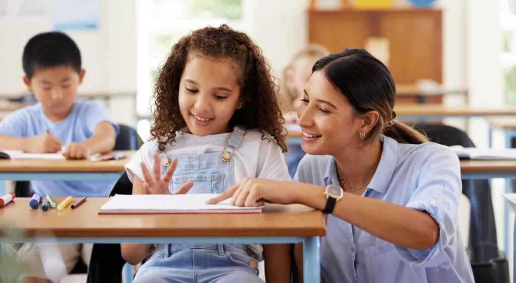 Teacher kneeling down helping a students at their desk