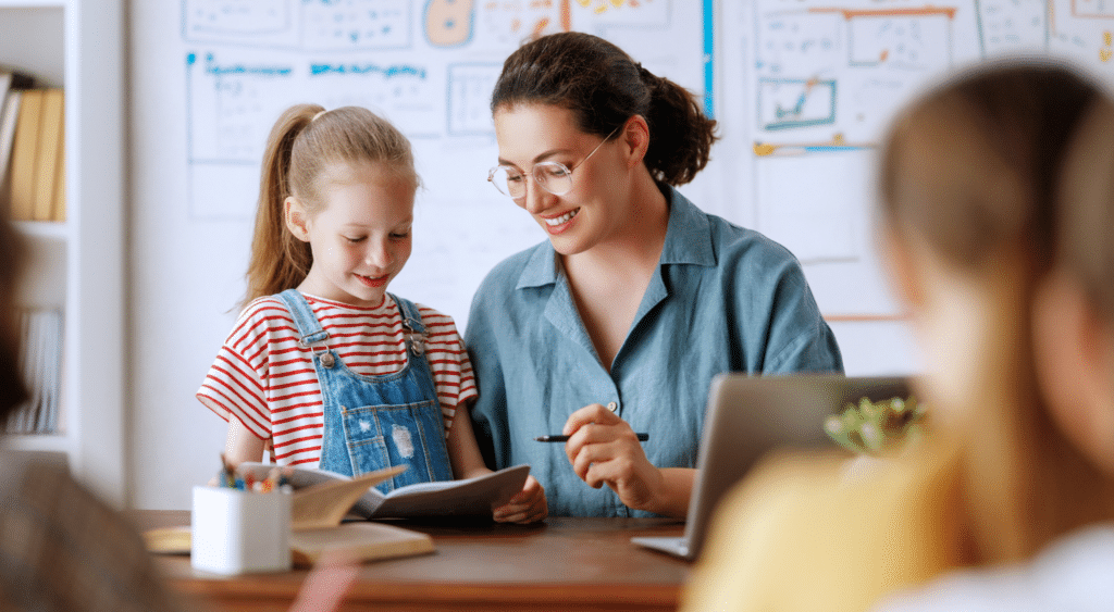 Substitute teacher sitting at desk looking over work with a student